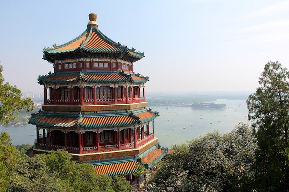 A traditional pavilion on a wooded hillside overlooking a calm lake.